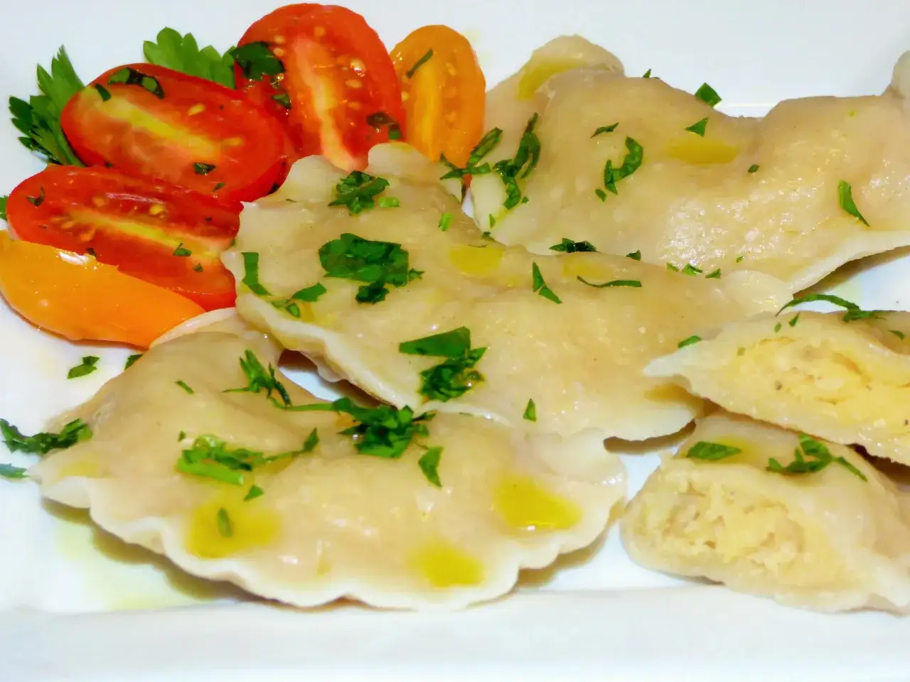 Pyszne pierogi z soczewicą czerwoną, polane oliwą i posypane natką pietruszki, podane z pomidorkami.