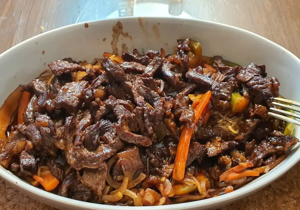 Pyszne wołowina stir fry z warzywami i makaronem, podane w białej misce.
