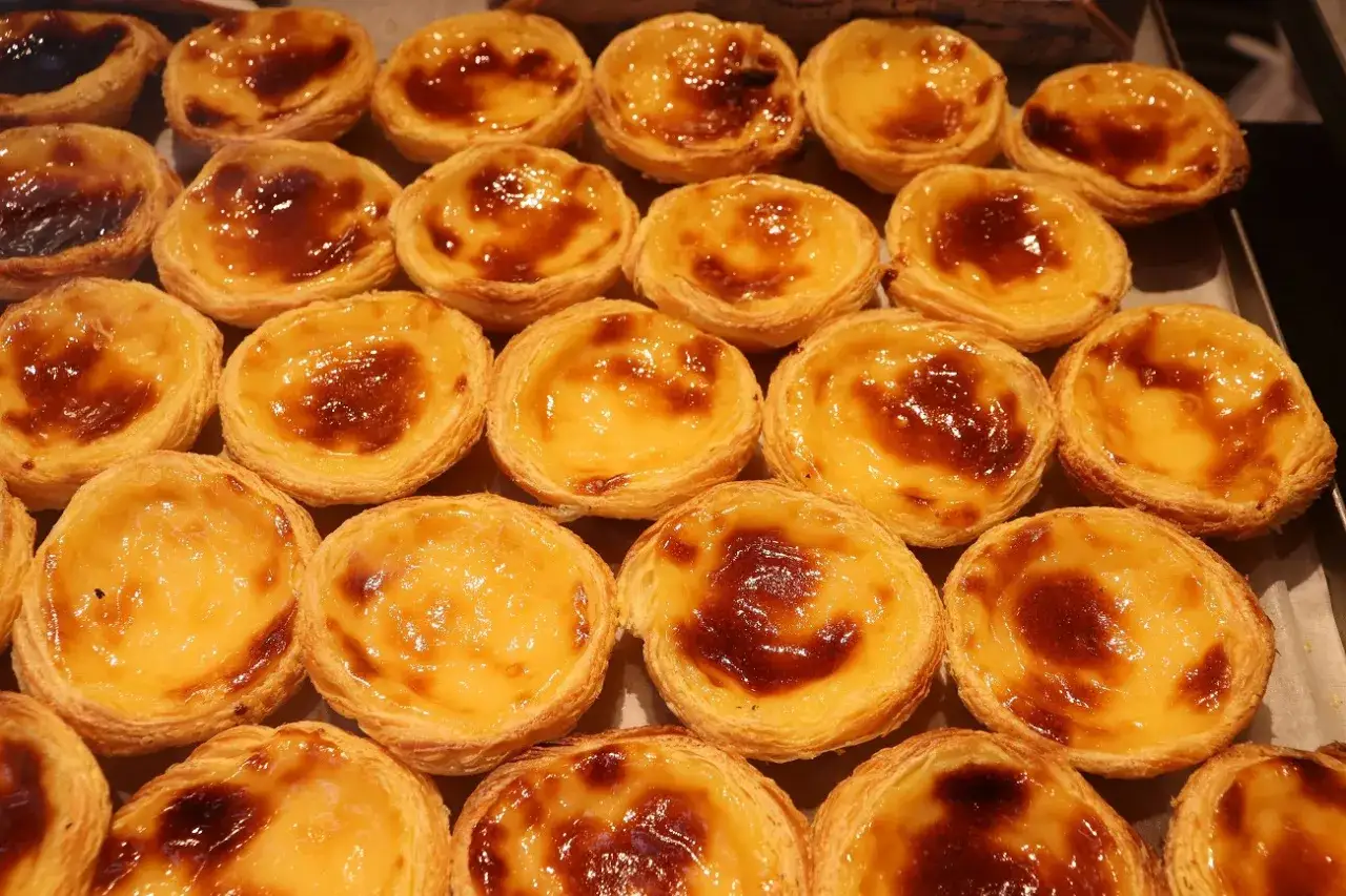 Taca z kremowymi, karmelizowanymi pastéis de nata, idealnymi na deser.