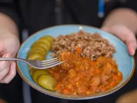 Pyszny gulasz z kaszą gryczaną i ogórkami kiszonymi na talerzu. Widok z bliska na kawałek mięsa nabierany widelcem.