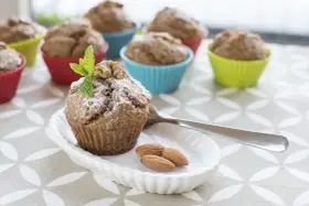 Pyszne muffinki bananowe fit, posypane cukrem pudrem, z orzechami i miętą. Obok migdały i łyżeczka.