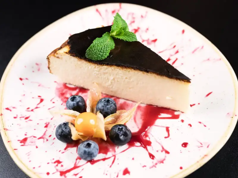 Kawałek sernika baskijskiego z palonym wierzchem, udekorowany borówkami, physalis i miętą. Idealny przepis na sernik baskijski.