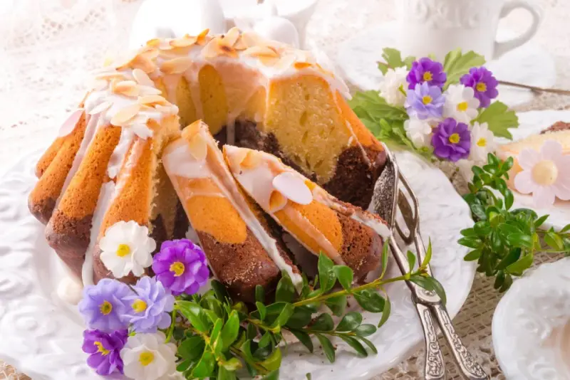 Modne ciasta na Wielkanoc: marmurkowa babka z lukrem i migdałami, ozdobiona wiosennymi kwiatami i zielenią.