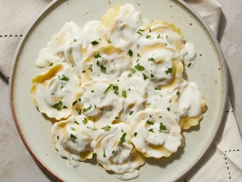 Ravioli w kremowym sosie, posypane natką pietruszki. Pyszny sos do ravioli, który zachwyca smakiem.